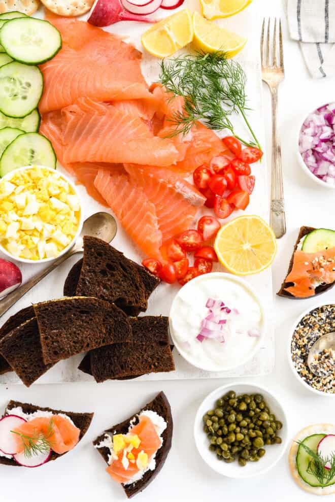 An appetizer platter with sliced lox, hard boiled egg, sliced cucumbers, chopped tomato, dill and brown bread.