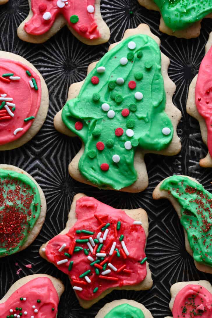 Frosted old fashioned sour cream cookies with sprinkles in a variety of shapes on a textured baking pan.