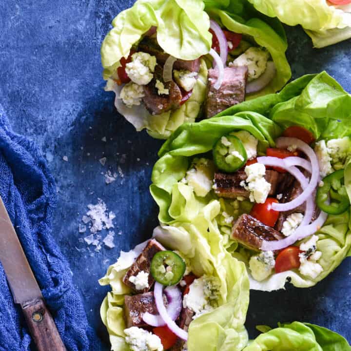 Butter lettuce leaves filled with steak, blue cheese, tomatoes and onions on a blue background.