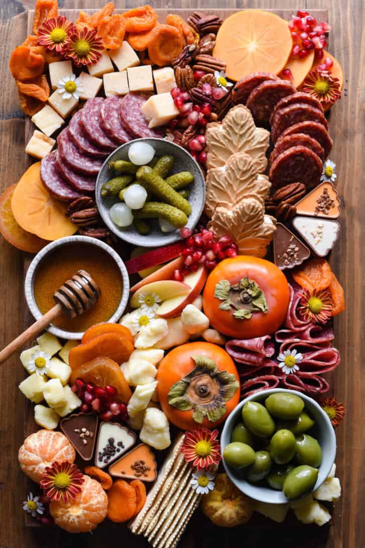 A Thanksgiving charcuterie board, including cured meats, cheeses, nuts, olives, fruit and crackers, arranged on a large wooden cutting board.