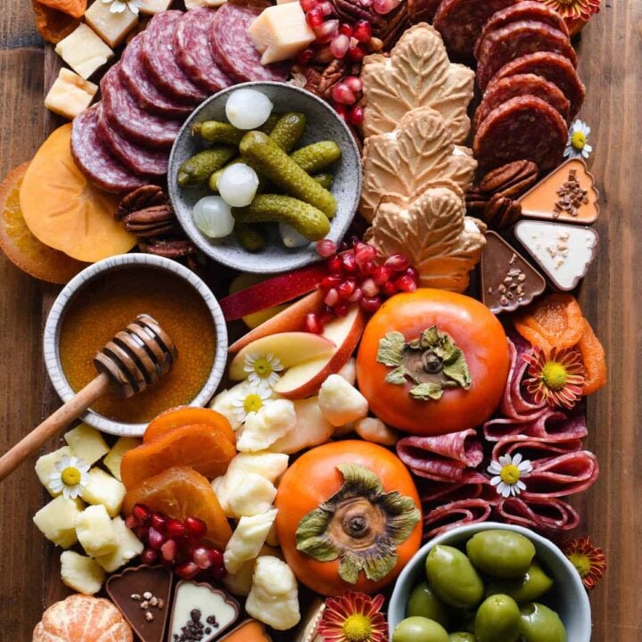 A Thanksgiving charcuterie board, including cured meats, cheeses, nuts, olives, fruit and crackers, arranged on a large wooden cutting board.