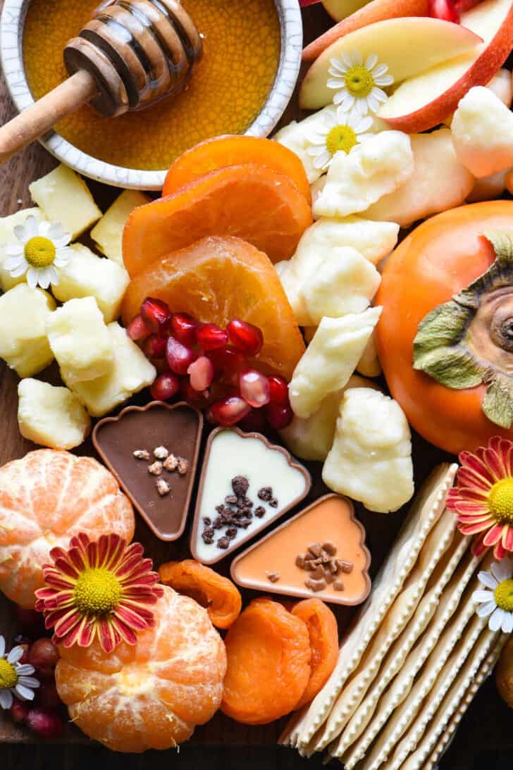 A cutting board spread with fruits, chocolates, crackers and cheese.