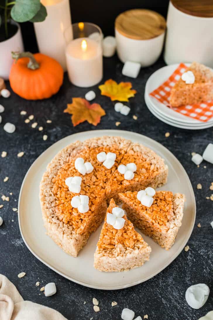 Thanksgiving Rice Krispies treats, shaped and cut into pie "slices," topped with marshmallows, on a round white plate.