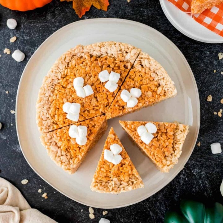 Thanksgiving Rice Krispies treats colored and shaped to resemble a pumpkin pie, on a white plate on a dark surface.