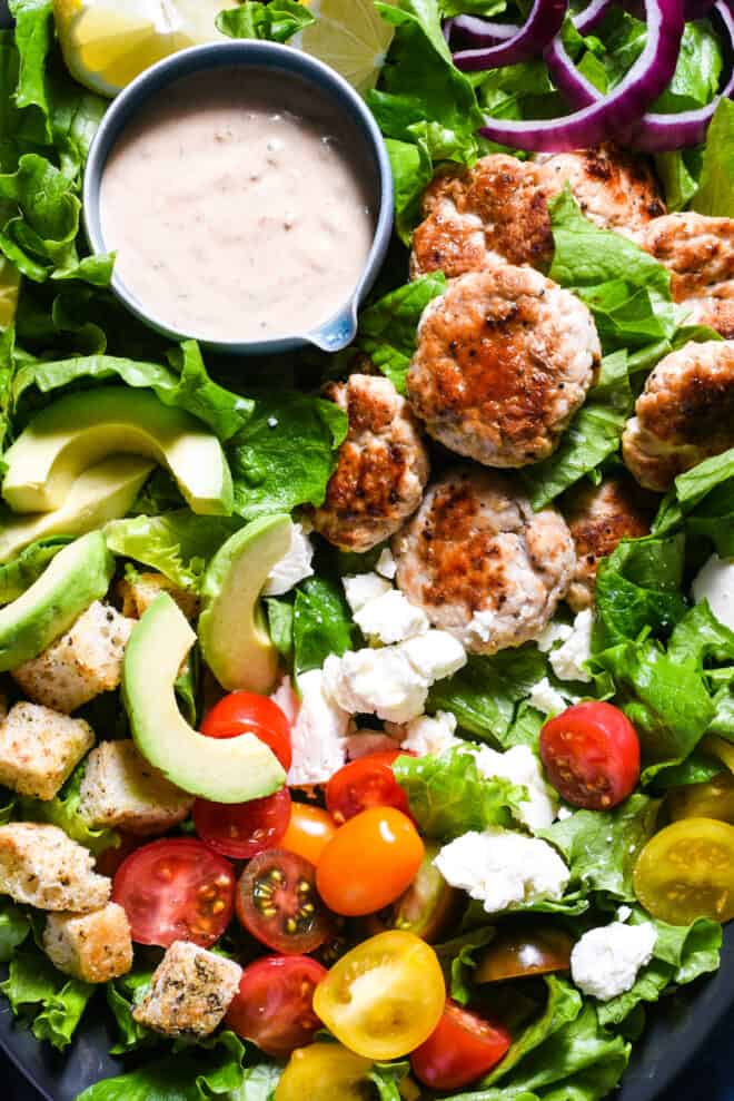 Turkey burger salad made with lettuce, small turkey patties, avocado, croutons, feta cheese, tomatoes and a creamy dressing.