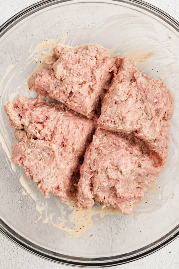 A raw ground poultry mixture in a glass bowl that has been scoured into 4 equal sections.