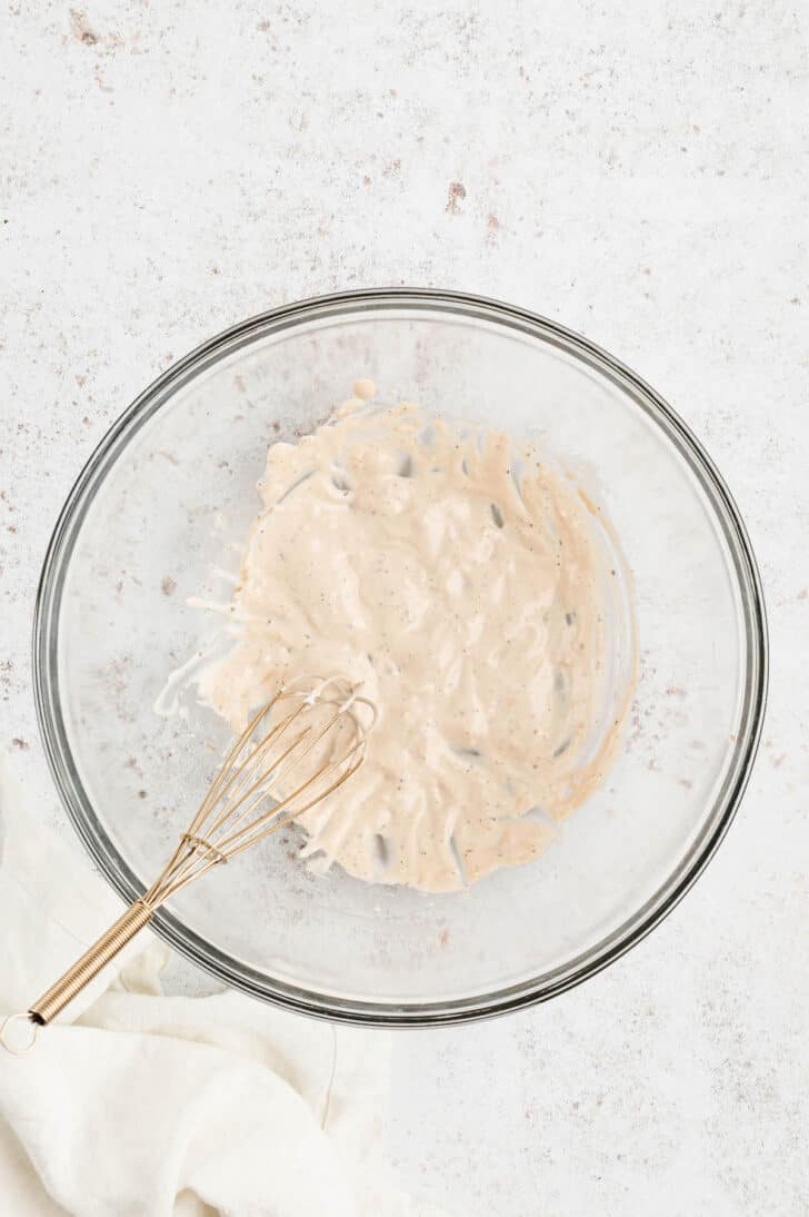 A glass bowl with a whisk combining mayonnaise with spices.