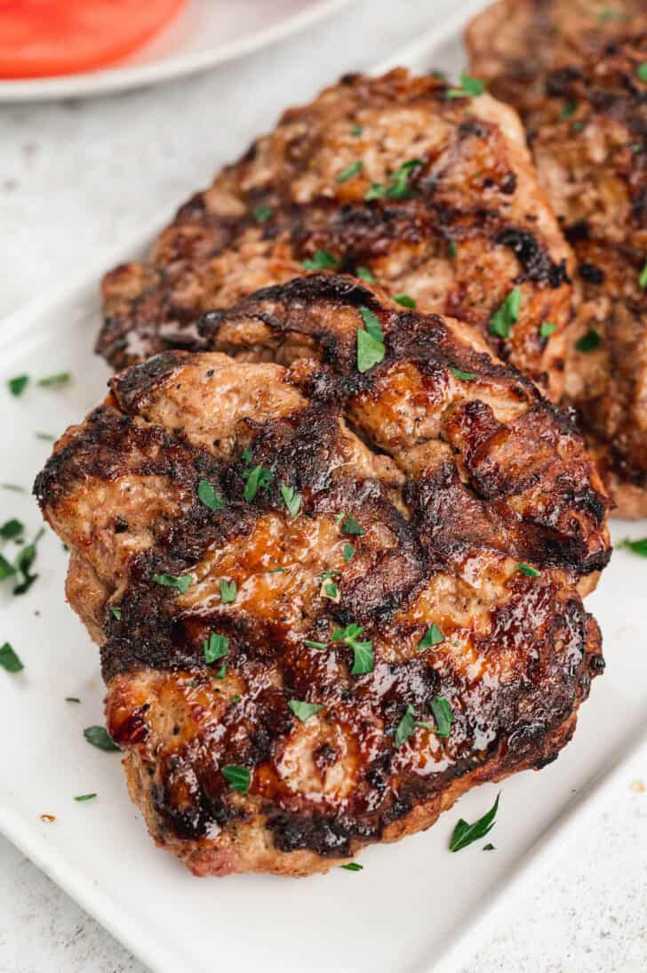 Cooked turkey burgers on a white plate sprinkled with parsley.