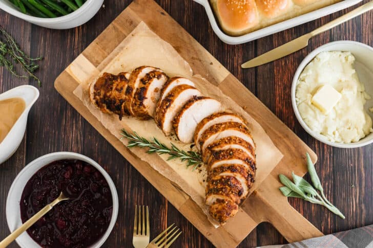 Sliced cooked poultry on a cutting board, garnished with rosemary.