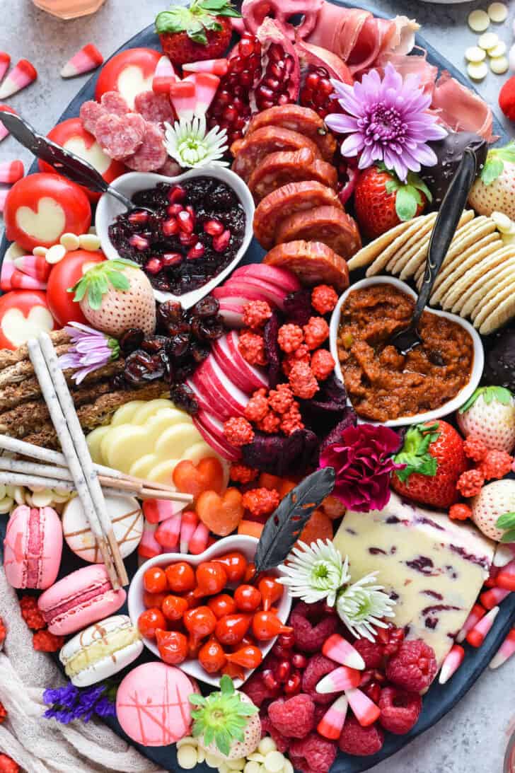 Large oval platter filled with red, pink and white Valentine's Day snacks, including cheese, charcuterie, fruits, vegetables, crackers and sweets.