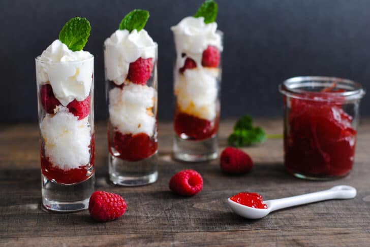 A Valentine's Day dessert made in three tall shot glasses, with layers of cake, raspberries, red jam and whipped cream.