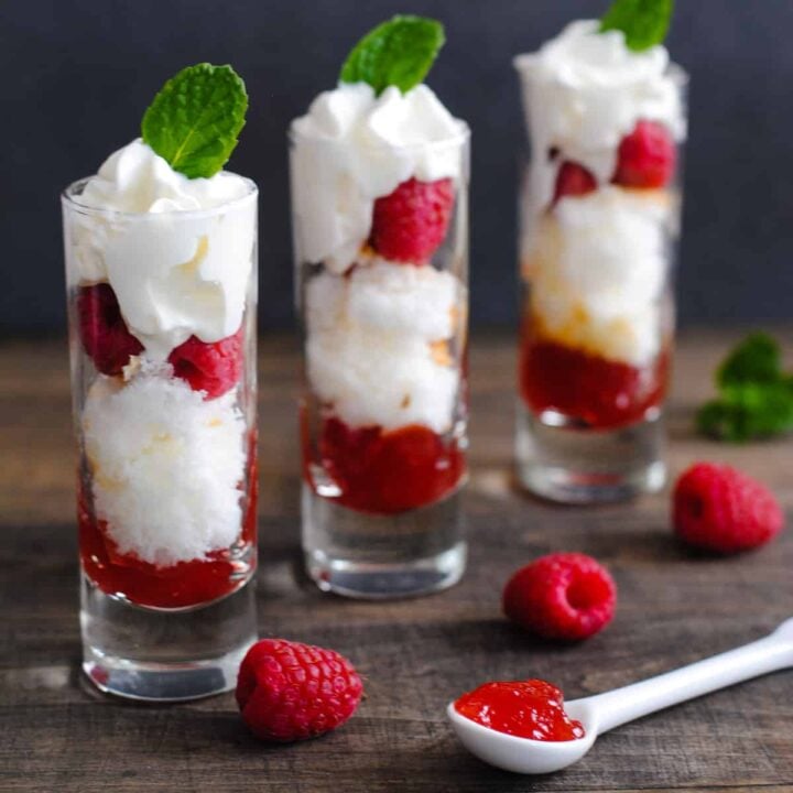 A Valentine's dessert made in three tall shot glasses, with layers of cake, raspberries, red jam and whipped cream.