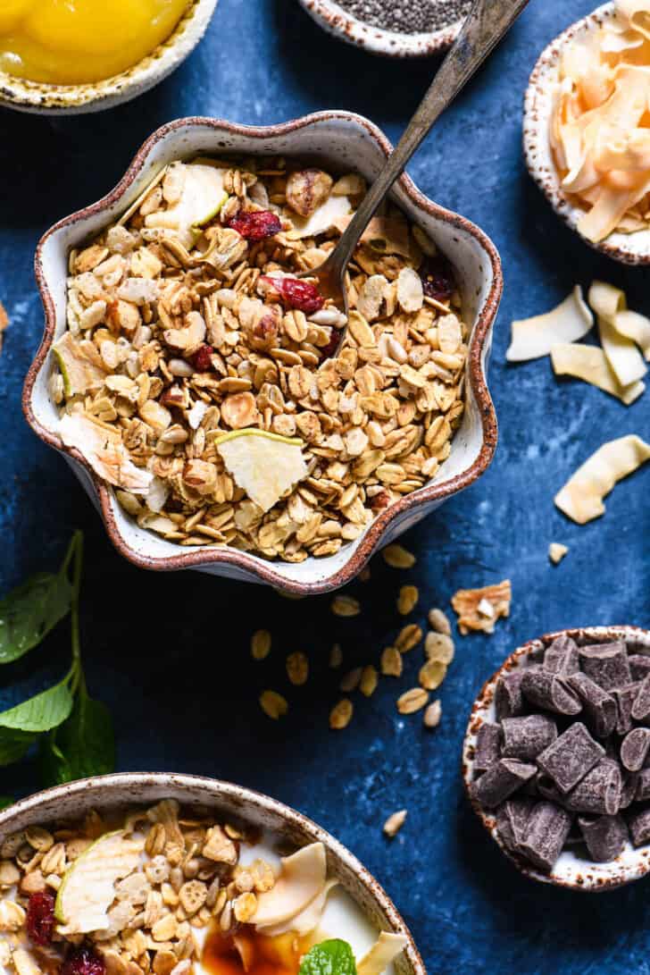 A bowl of granola as part of a yogurt parfait bar on a textured blue surface.